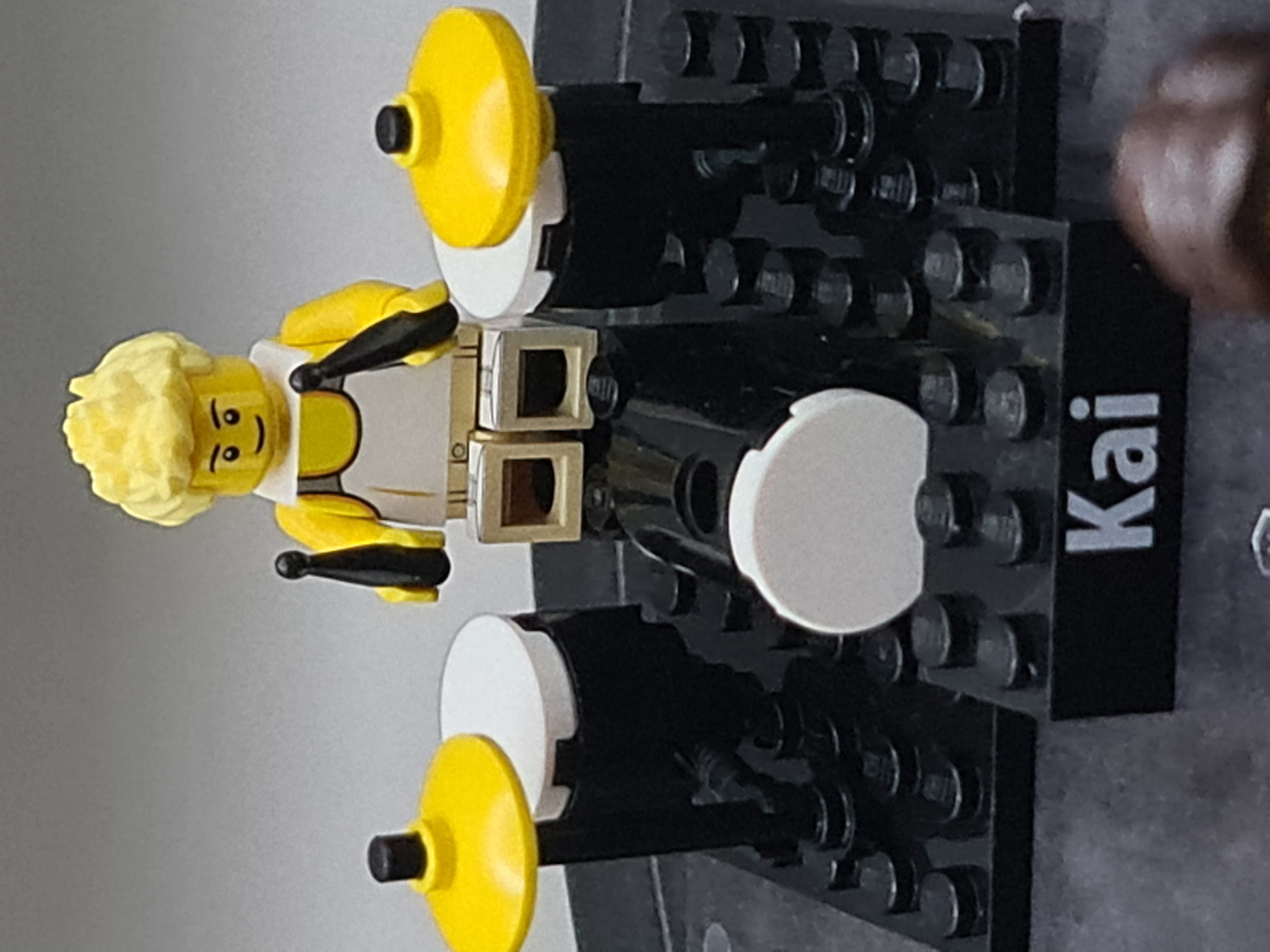 Kai is represented by a Lego figure in classic Lego yellow. Kai is playing a Lego drumkit.